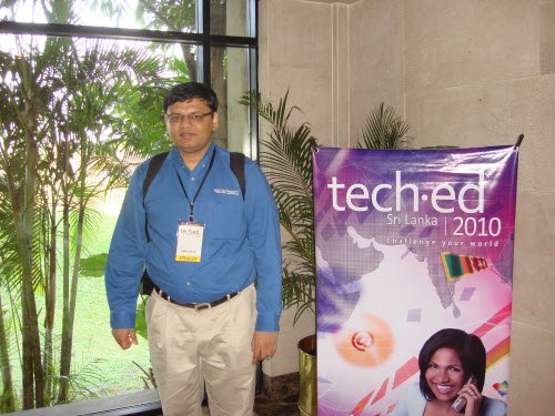 Pinal Dave in a blue shirt and a name badge, standing beside a TechEd Sri Lanka 2010 banner
